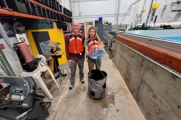 Two 主要研究 student researchers hold their winning ocean renewable energy device in front of a wave tank. 他们穿着红色的救生衣.